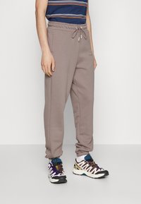 Ljust bruna sweatpants med elastisk midja och dragsko. Har sidofickor och avsmalnande ben. Kombinerat med färgglada träningsskor.