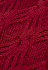 Gebreide stof in diep rood met een gestructureerd, verweven patroon met duidelijke kabels en gladde secties. Zachte, dikke garen gebruikt.