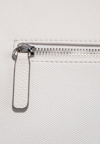 Hvid tekstureret stof med en metalsk_zipper. Zippertrækkeren er lavet af glat læder. Har en sølvfinish på metaldele.
