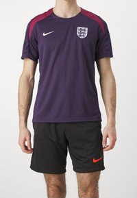 Lila Nike träningsskjorta med vinröda axelaccentuer, prydd med England fotbollens logotyp och vit swoosh; tillsammans med svarta shorts.
