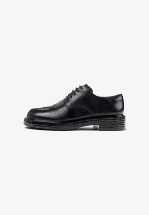 Black leather dress shoe with a round toe, lace-up design, textured side accents, and a layered, chunky black sole.