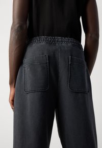 Dark gray pants with an elastic waistband, two back pockets, and a smooth texture, shown from the back against a neutral background.