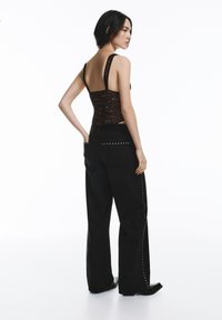 Fekete csipkés body széles pántokkal, magas derekú sötét farmernadrággal párosítva, ezüst szegecsekkel az oldalsó varrások mentén.