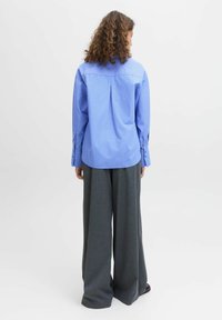 Camisa de cuadro azul claro con manga larga y puños abotonados, combinada con pantalones grises de pierna ancha. Tela suave con un ajuste relajado.
