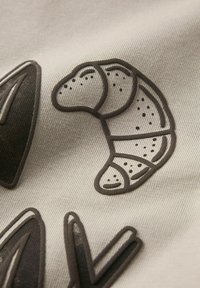 Beige stof met een gedetailleerde bruine afbeelding van een croissant met gestipte accenten, naast abstracte vormen en lijnen.