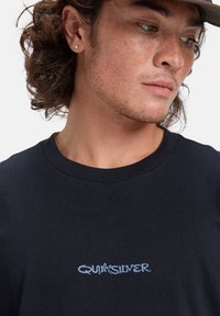 Black cotton t-shirt featuring a blue logo "QUIKSILVER" at the chest, round neckline, and short sleeves. Smooth texture, casual design.