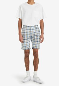 White short-sleeve t-shirt with a pocket, paired with blue and brown plaid shorts. Shoes are white, and socks are light-colored.