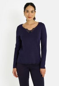 Suéter de manga larga color azul marino con cuello en V decorado con un delicado borde de encaje negro. Material suave con una silueta ajustada.