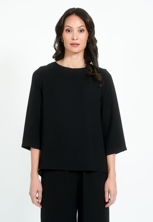Črn kratkosleeven top z okroglo izrezom in sproščenim krojem. Narejen je iz gladkega blaga z rahlo teksturo in ima raven rob.
