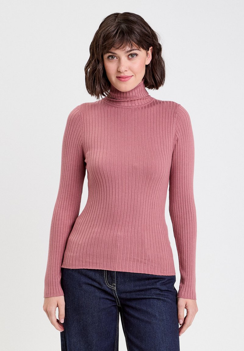 Maglione a collo alto a coste in rosa polveroso, design aderente con maniche lunghe, caratterizzato da un tessuto texture e un colletto alto. Abbinato a denim scuro.