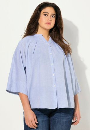 Camicia azzurra chiara, oversize, con colletto a punta, parte anteriore plissettata e maniche corte larghe. Tessuto liscio, design informale.