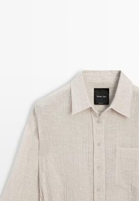 Beige textured long-sleeve button-up shirt with collar and chest pocket, labeled Massimo Dutti.