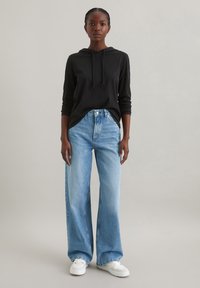 Zwarte hoodie met een vo zak en trekkoord, gecombineerd met lichtblauwe wijde spijkerbroek en witte sneakers. Minimalistisch ontwerp, casual pasvorm.