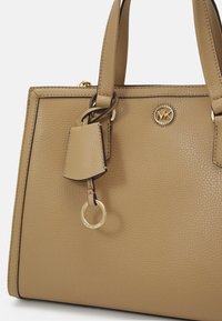 Sac à main en cuir tan avec une finition texturée, forme carrée, accents en métal doré et détail de logo. Inclut une étiquette décorative et un porte-clés.