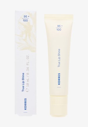 Korres True Lip Shine w miękkim beżowym opakowaniu (10 mL) obok eleganckiego białego pudełka z subtelnymi graficznymi wzorami i niebieskim tekstem.