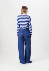 Rutet langermet skjorte i blå og hvit, kombinert med høyt liv vide blå jeans. Har baklommer og et enkelt svart midjebånd.