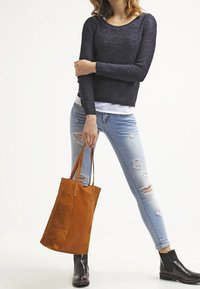 Tan läderhandväska med två handtag, tillsammans med en mörkblå stickad tröja och ljusblå slitna jeans. Svarta ankelstövlar synliga.