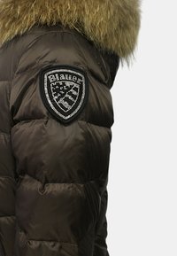 Giacca puffer marrone con cappuccio rifinito in pelliccia, con una toppa decorata con strass sulla spalla. Tessuto lucido e texture. 
