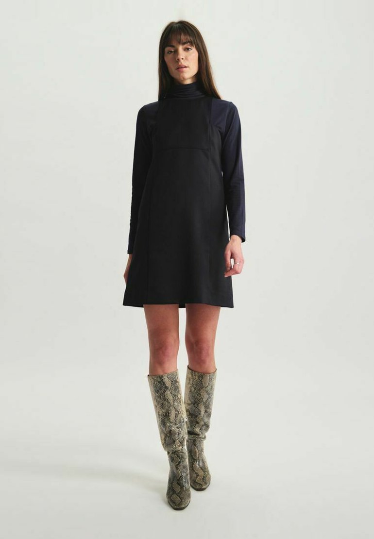 Robe noire sans manches avec un corsage ajusté et une jupe évasée, associée à des bottes en cuir à motif serpent montant jusqu'aux genoux. Texture de tissu lisse.