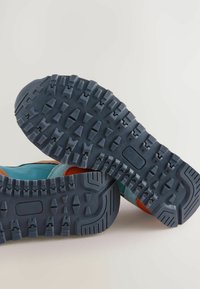 Mehrfarbige Schuhe mit einer blauen Gummisohle, die tiefe Rillen aufweist, Wildlederakzenten in Blau und Orange sowie einem leichten Design.