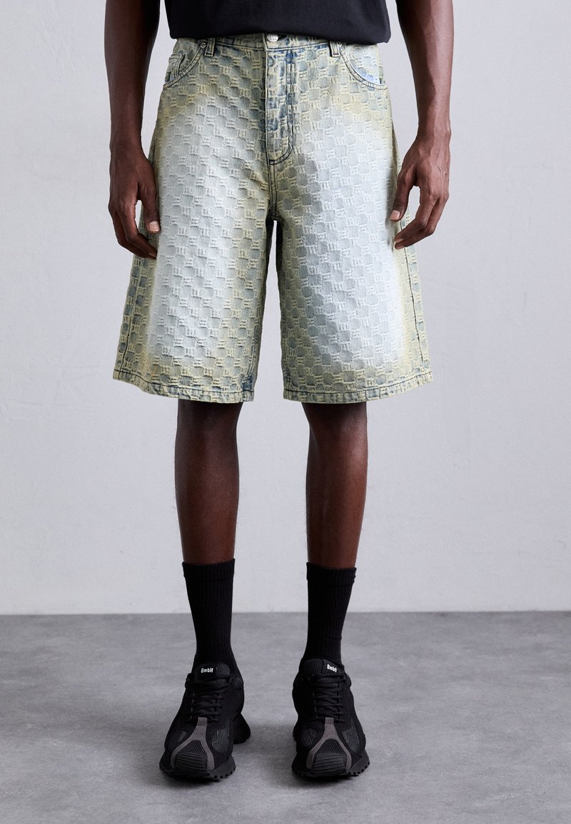 Shorts en denim avec une texture à motifs, présentant un dégradé bleu et jaune délavé. Longueur genou avec une taille standard et cinq poches.