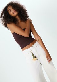 Brun bandeau-topp, vita vida jeans med en dekorativ nyckelring som har en blomma och en klocka. Lockigt hår och en synlig arm-tatuering.