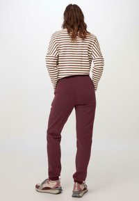 Gestreiftes Langarmoberteil in Creme und Burgunder, kombiniert mit burgunderfarbenen Jogginghosen. Ergänzungen sind hellfarbene Sneakers mit pinken Akzenten.