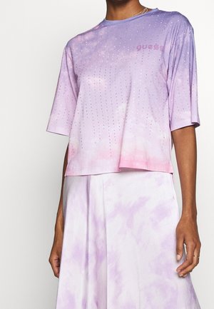 Woman wearing a light purple and pink gradient short-sleeve top with small rhinestones and matching wide-leg pants.