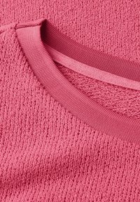 Nahaufnahme eines rosafarbenen gestrickten Pullovers, der den strukturierten Stoff und den gerippten runden Ausschnitt zeigt.