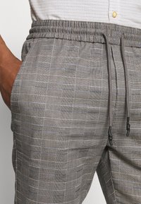 Pantaloni da uomo grigi a quadri con vita elasticizzata e coulisse. Presentano sottili linee blu e rosse in un tessuto testurizzato.