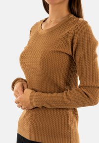 Maglione marrone in stile texture con un motivo a trecce, maniche lunghe, polsini a costine e bottoni decorativi sulla spalla.