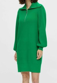 Robe tricotée verte avec un col montant et une fermeture à glissière, des manches longues ballon et une coupe décontractée, arrivant à mi-cuisse.