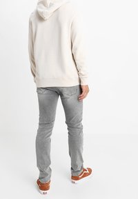Ljusbeige hoodie med snörning, i kombination med grå slim-fit jeans. Bruna skodon med vita sula. Minimalistisk design, inga synliga mönster.