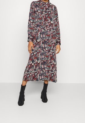Femme portant une robe midi à manches longues, à motifs abstraits rouges, blancs et noirs, associée à des bottines noires à talons.