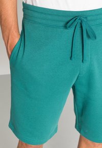 Pantaloni corti turchesi in cotone con vita elastica e coulisse, dotati di tasche laterali e una texture liscia.