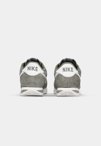 Sivé semišové tenisky Nike s bielymi doplnkami, s textúrovaným zadným dielom, logom na päte a viacvrstvovým dizajnom podrážky.