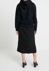 Svart hoodie med en stor huva, kombinerad med en svart knälång kjol. Texturerad tyg och klackskor med blockklack fulländar outfiten.