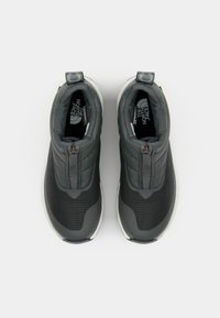 Sorte og grå glidelåssneakers med teksturert overdel, rund tå og en polstret såle. Har en løkke ved hælen for enkel påkledning.