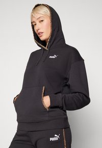 Hoodie noir avec une bordure en imprimé léopard sur la capuche et les poches, doté d'une poche kangourou à l'avant et d'un logo Puma blanc sur la poitrine.