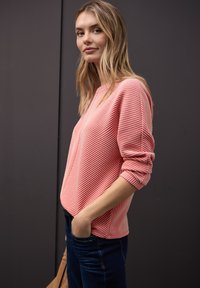Suéter a rayas rosa con cuello redondeado y mangas dobladas, combinado con jeans oscuros. La tela parece suave y texturizada.