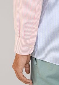 Gestreept overhemd met roze en blauwe verticale strepen, met een witte knoopmanchet en een lichtgewicht gevoel. Draagt een mintgroene broek.