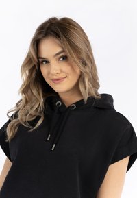 Zwarte mouwloze hoodie met een capuchon en een trekkoord en metallic accenten. De stof lijkt zacht met een gladde textuur.