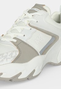 Baskets blanches et grises avec panneaux en mesh et cuir, semelle épaisse, lacets et logo MK sur le côté.