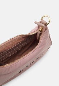 Měkká růžová nylonová kabelka se zlatým zipem, vnitřní kapsou a kontrastním hnědým podšívkou. Disponuje vrchním popruhem a logem na vnějším povrchu.