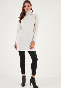 Lys grå strikket turtleneck kjole med ribbede kanter, båret over sorte leggings og høje ankelstøvler. Lange ærmer, slank silhuet.