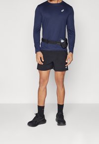 Laivaston pitkähihainen urheilupaita, mustat shortsit, mustat juoksukengät ja juomavyö pullolla. Suunnittelu on suoraa, tiukkaa kangasta, käytännöllinen design.
