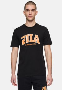 Svart bomullströja med en iögonfallande orange FILA-logotyp och texten "Etablerad 1911". Korta ärmar och rundad halsringning.