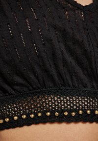 Top scurt negru, realizat dintr-un material texturat cu dungi verticale, cu un tiv din croșetă și studs decorative de culoare aurie pe margine.