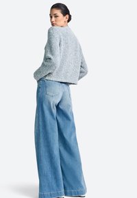 Modrý svetlý krátky sveter s textúrou, v kombinácii s širokými nohavicami z ľahkých modrých riflí, zobrazený na jednoduchom sivom pozadí.