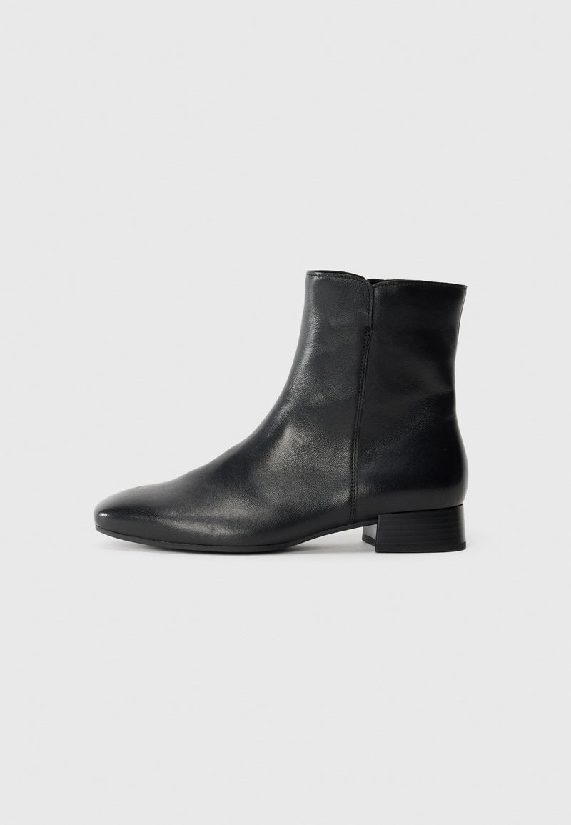 Bota negra de cuero hasta el tobillo con tacón bajo y cremallera lateral sobre un fondo liso de color gris claro.